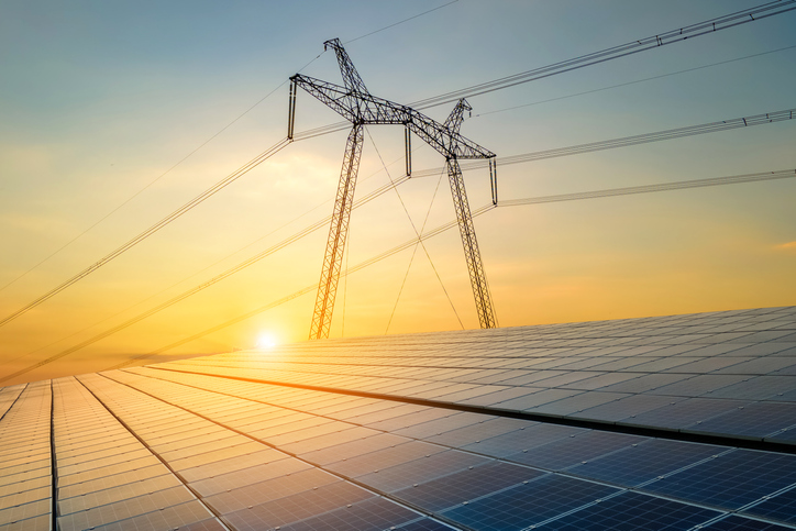 High voltage pylons with electric power lines transferring electricity from solar photovoltaic sells at sunrise.